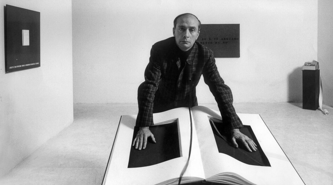 Man in plaid shirt leaning over oversized open book sculptures in a gallery.